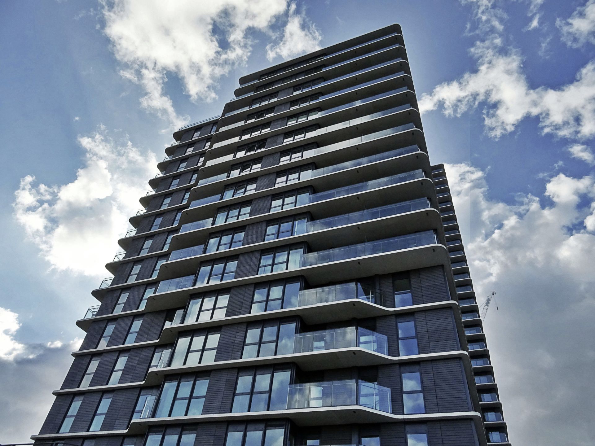 Low-angle shot of a modern glass skyscraper against a blue sky with white clouds