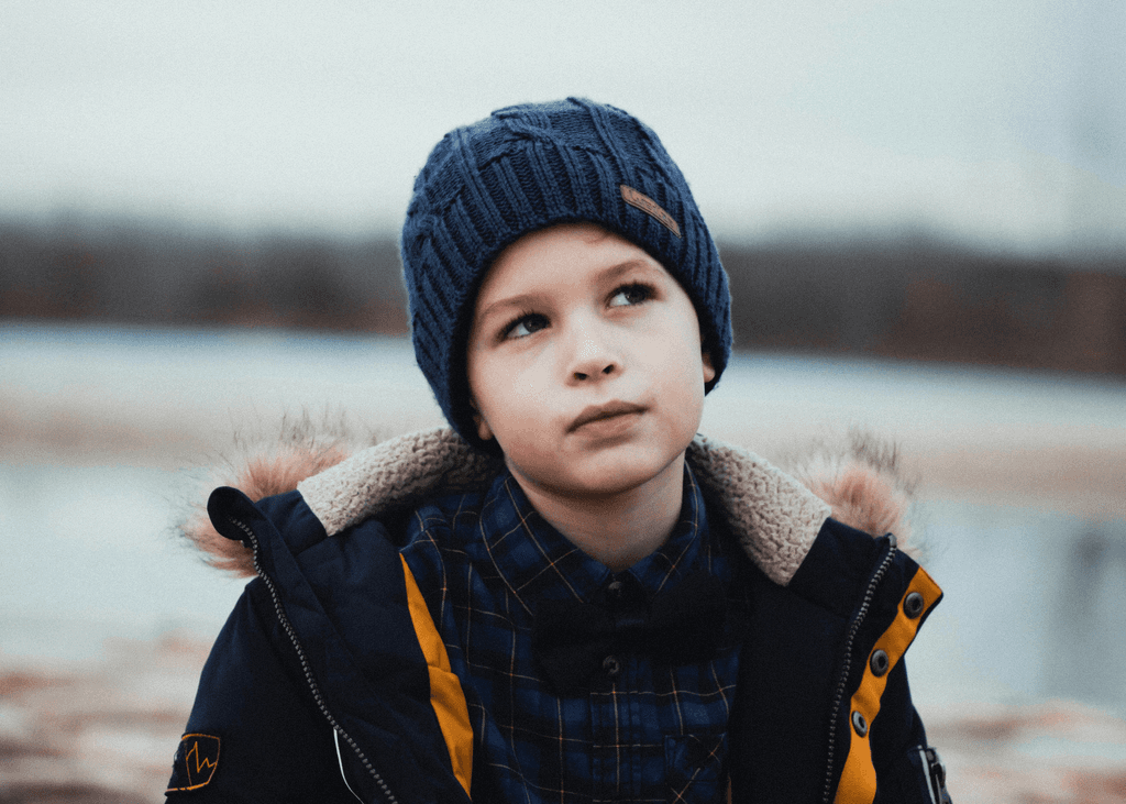boy in black and yellow jacket and knit cap standing near body of water during daytime