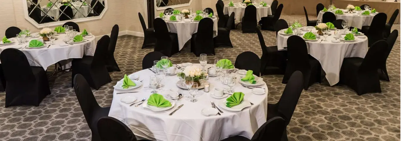 Event room with white-clothed round tables, black chairs, and green napkins.