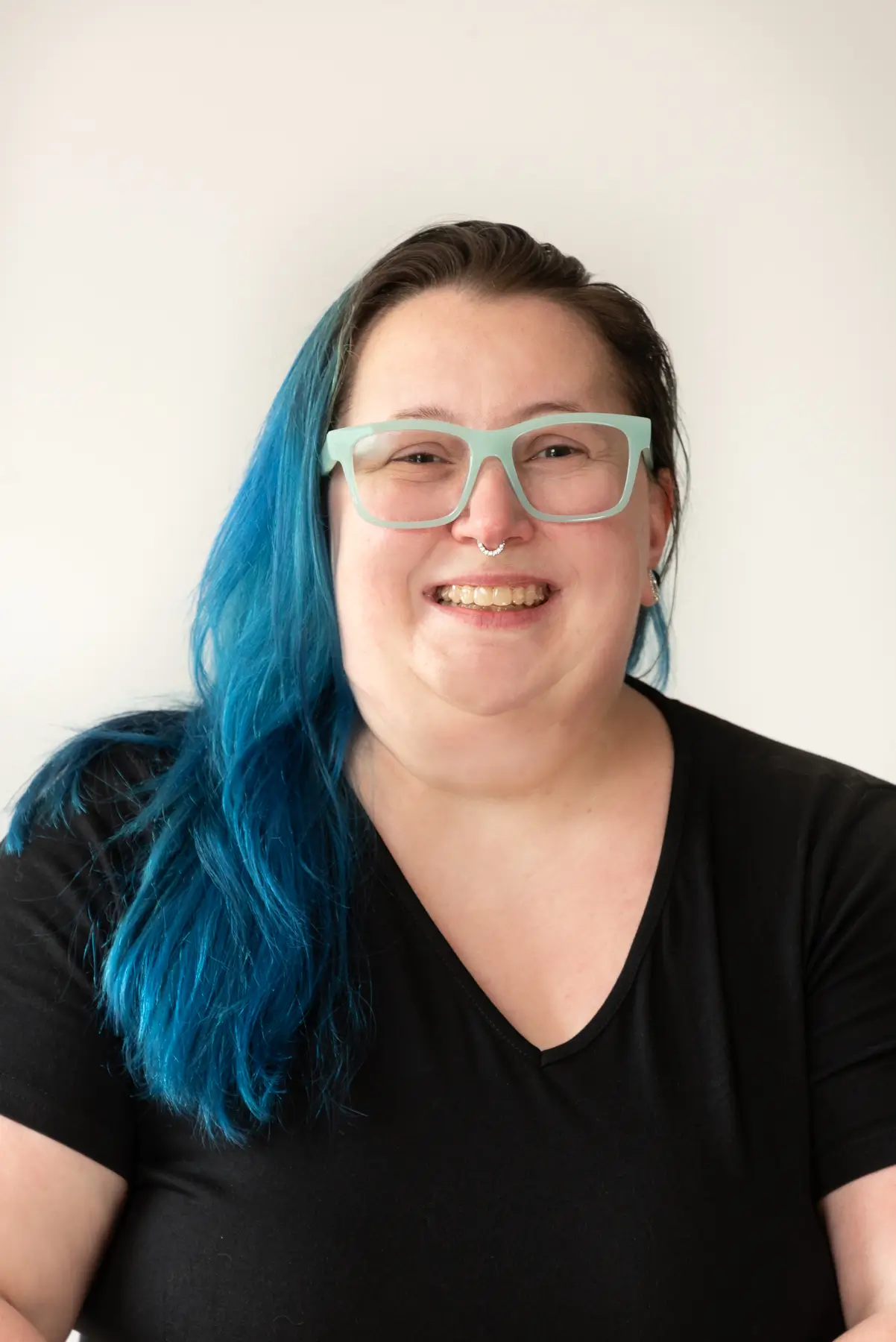 Smiling woman with vibrant blue hair and light green glasses in a portrait.