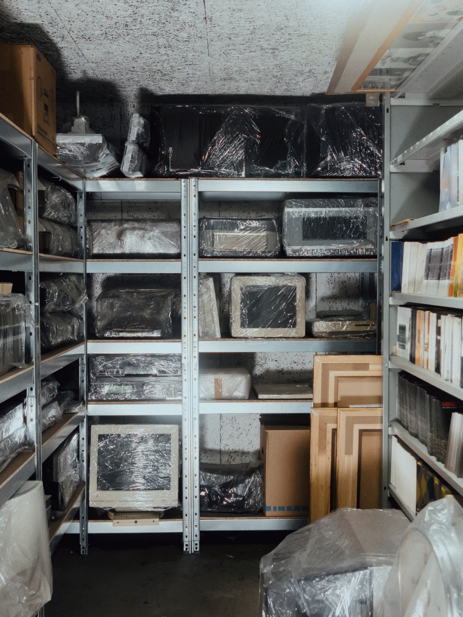 Photo d'une salle des archives du label de musique italien PDU montrant du matériel informatique emballé dans du papier cellophane et rangé sur des étagères métalliques