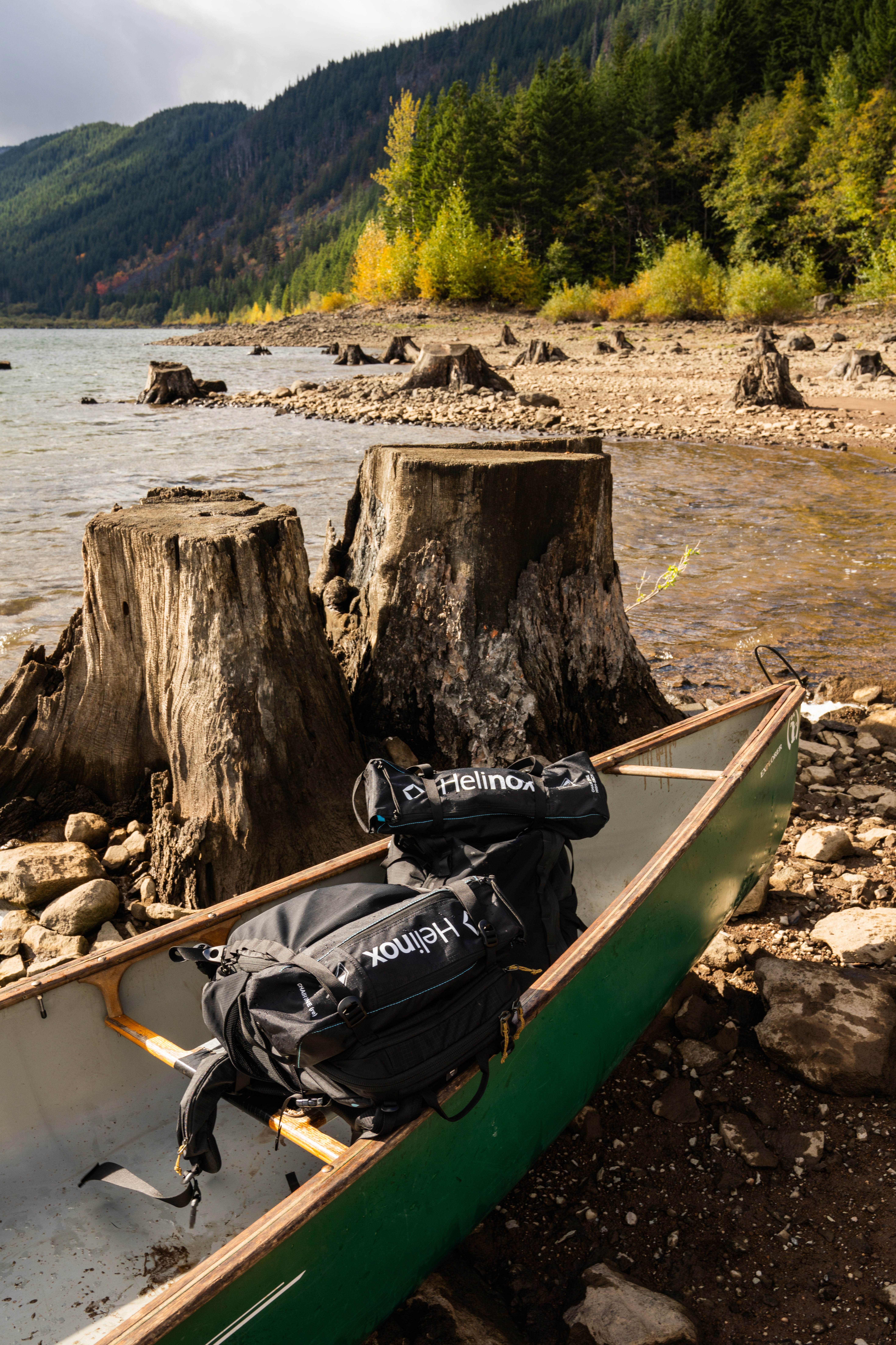 Sur un kayak lelong d'une rivière, sont posés des sacs de matériel de camping Helinox