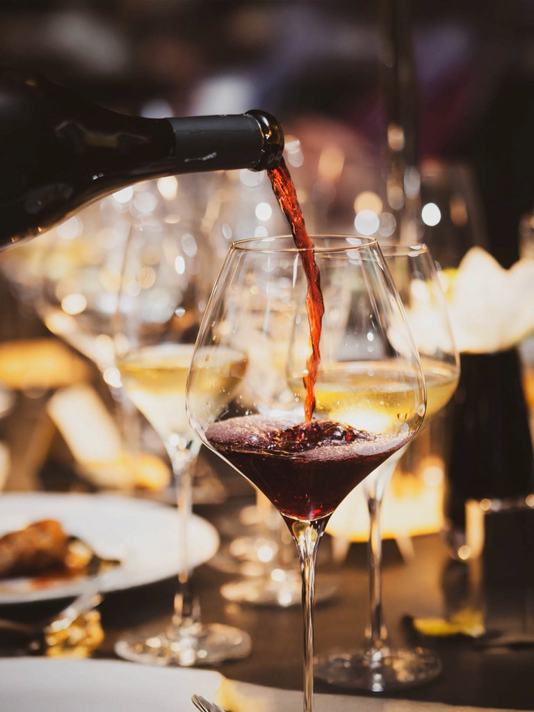 Red wine being poured into a glass at a formal dinner setting.