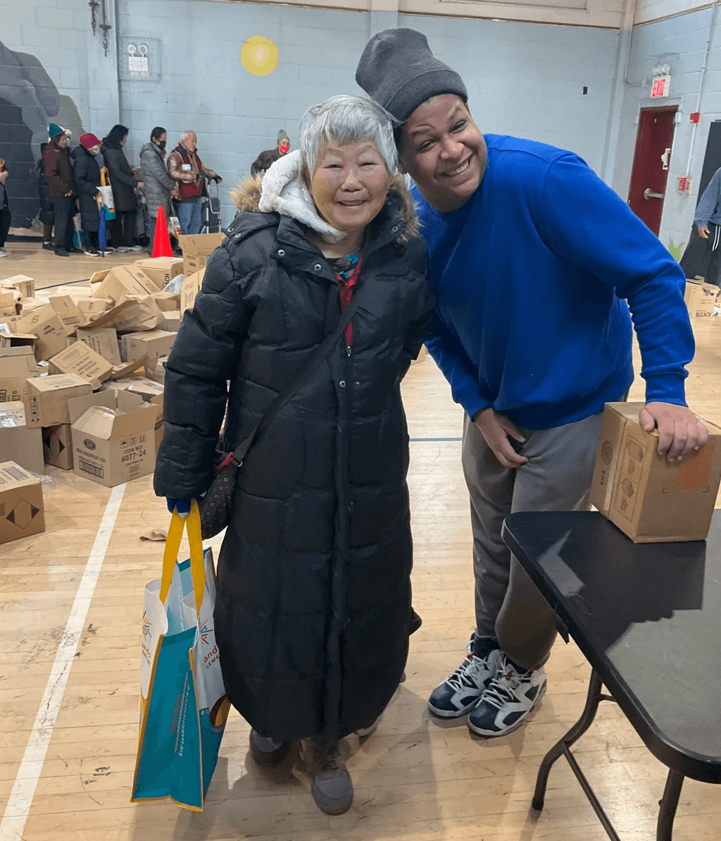 A volunteer poses with a Grand Street Senior who carries a bag of donations.