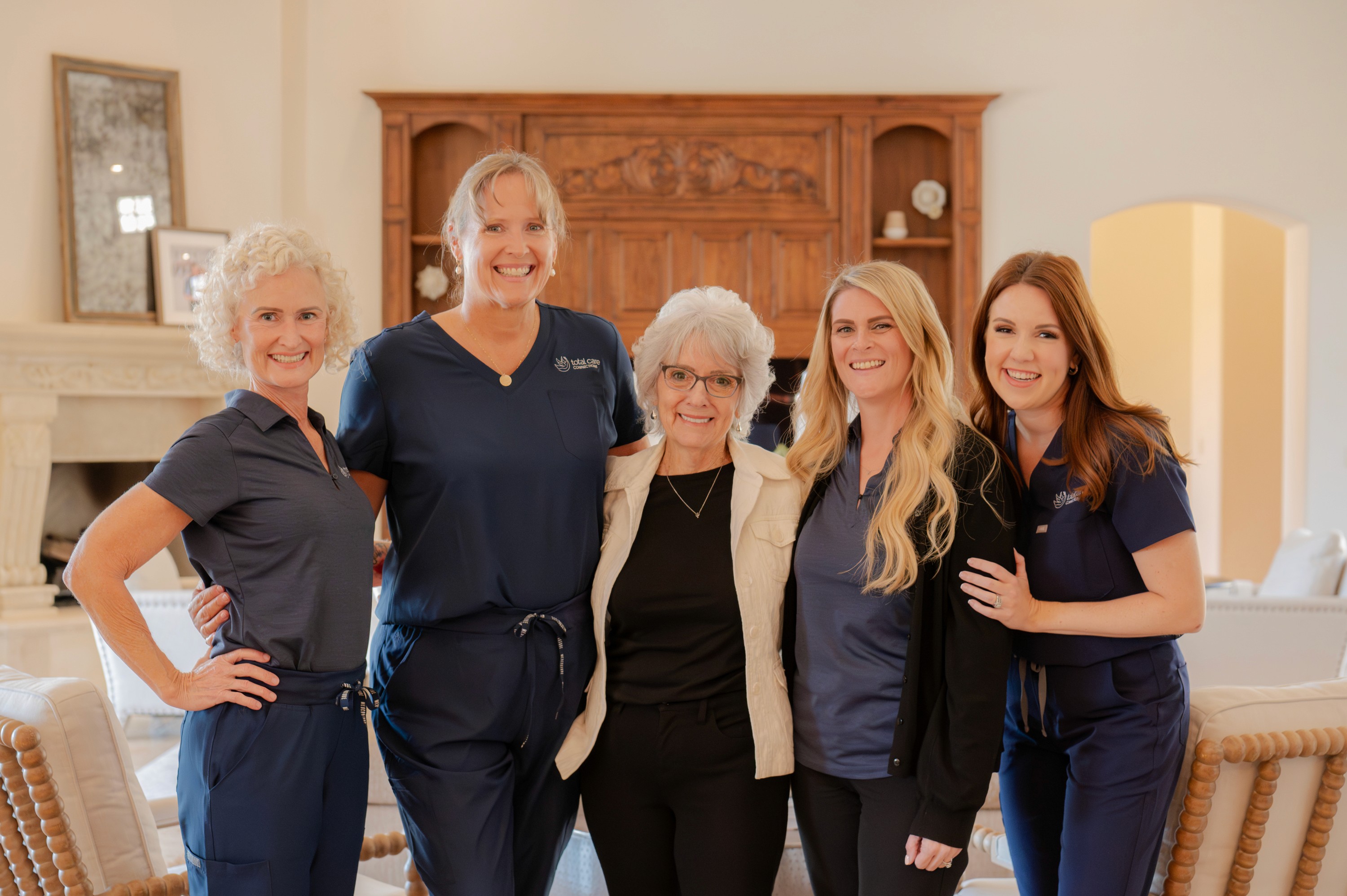 Five women, smiling and standing together indoors.