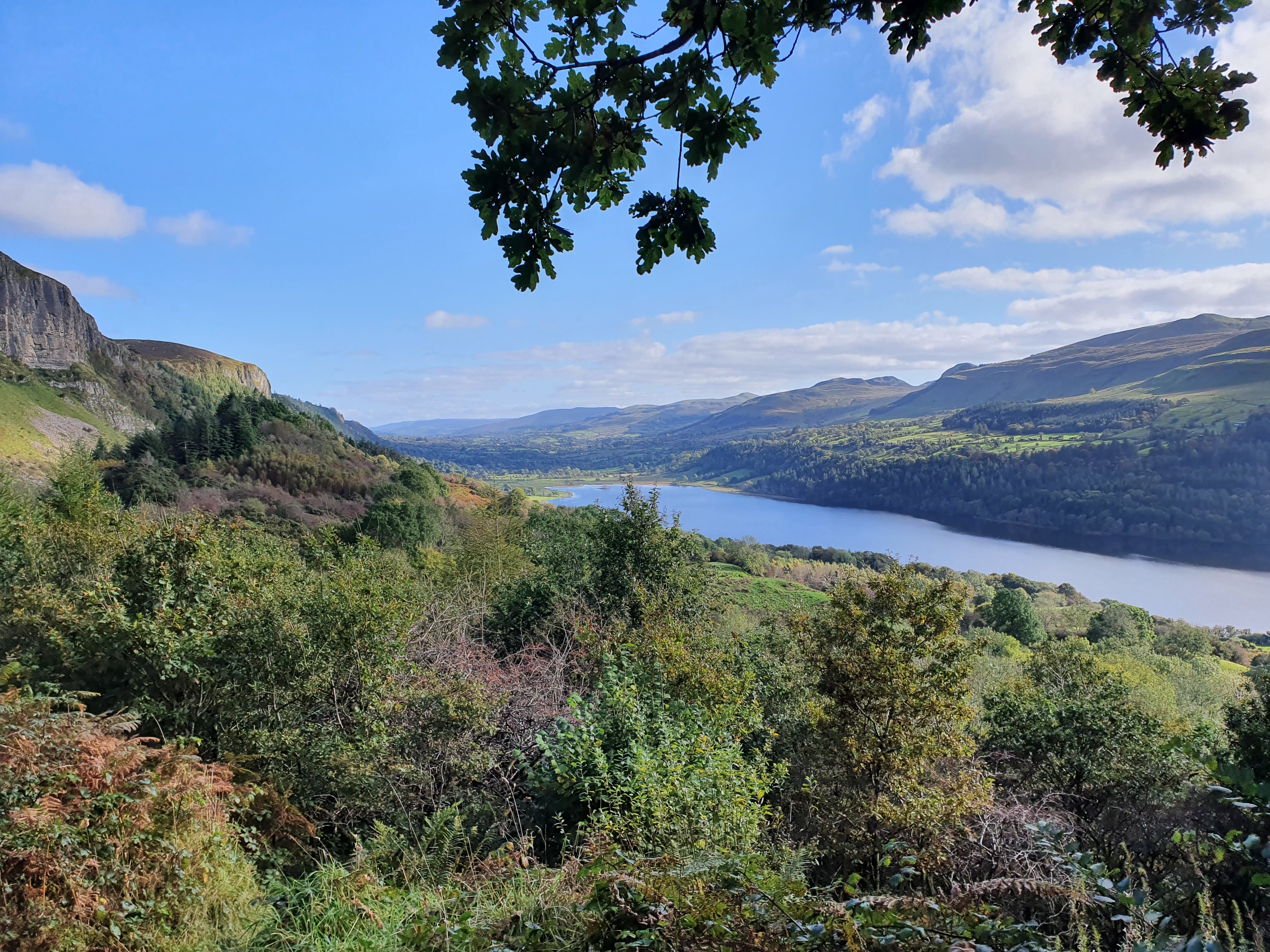 A scenic landscape view featuring a river surrounded by green hills under a partly cloudy sky.