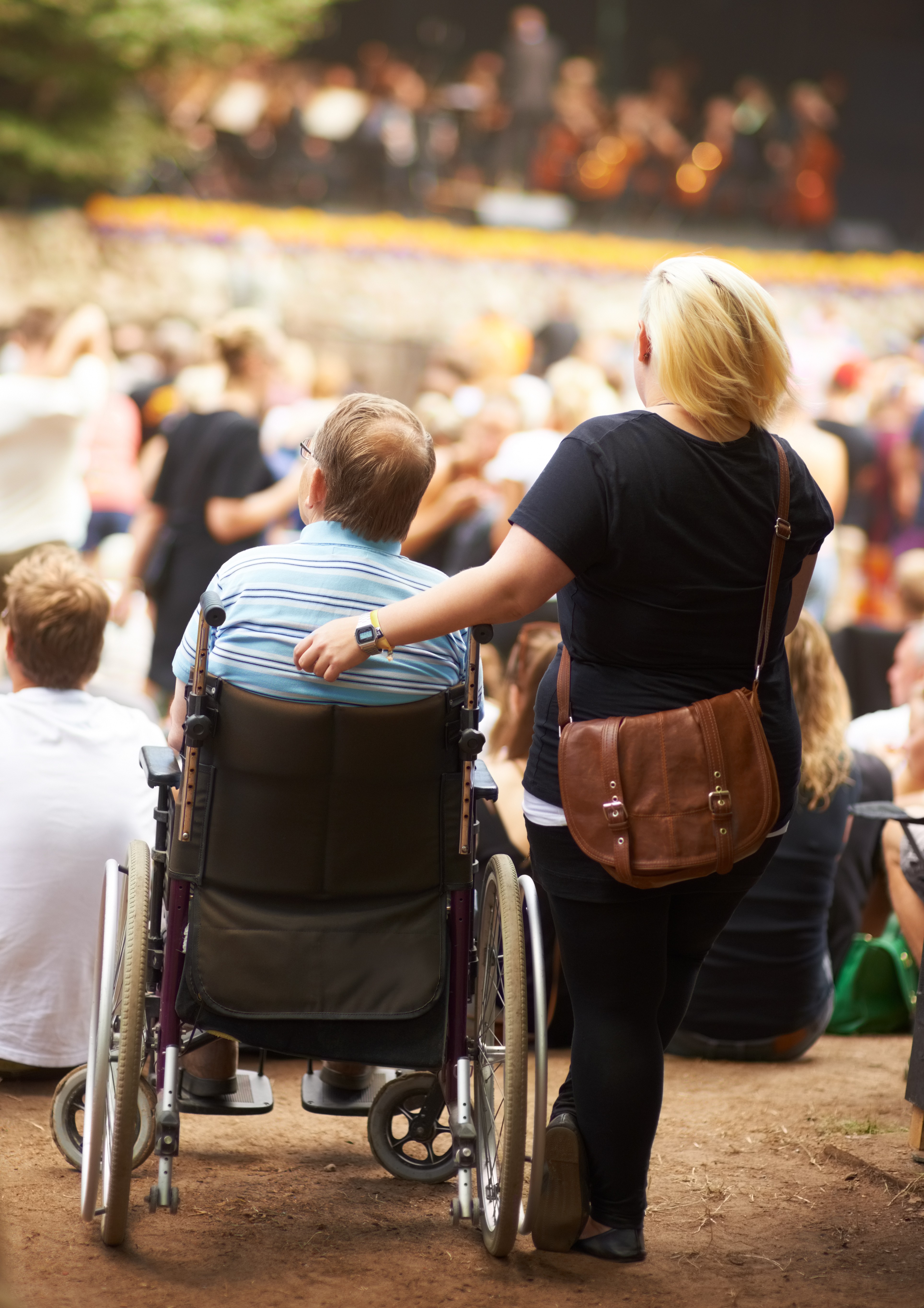 Attendant supporting a wheelchair user in a crowded outdoor event audience