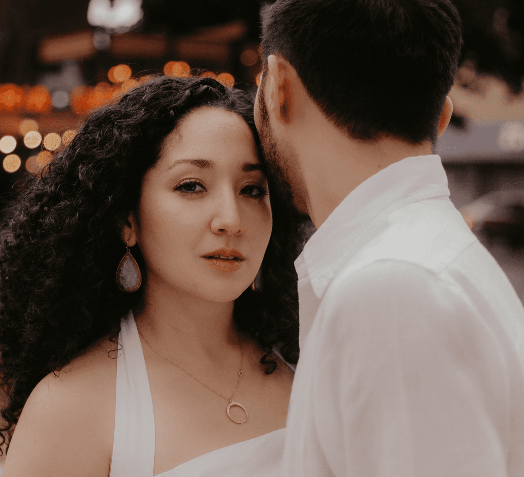 A close-up of two people holding hands, one wearing a denim jacket. The background is softly blurred, suggesting a tender, intimate moment in warm light.