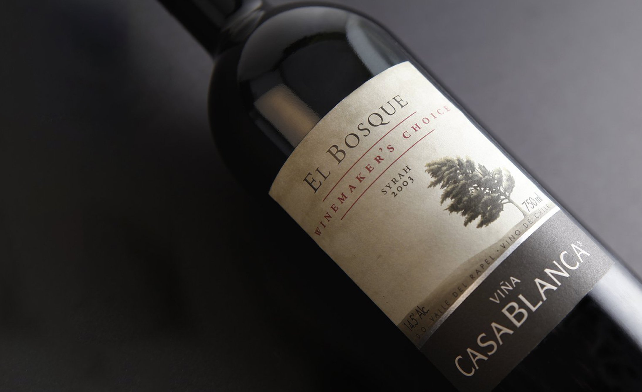 Bottle of El Bosque Syrah 2004 wine from Viña Casablanca, lying on a dark surface. The label features a tree illustration, conveying elegance.