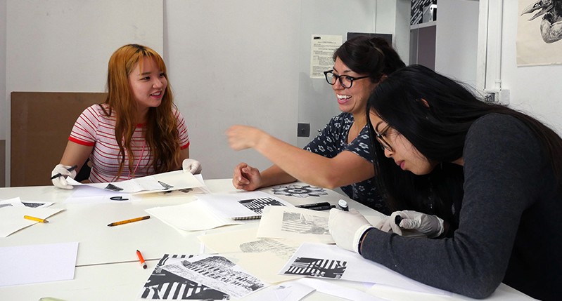 Students meticulously working on different drawing designs while talking to each other.