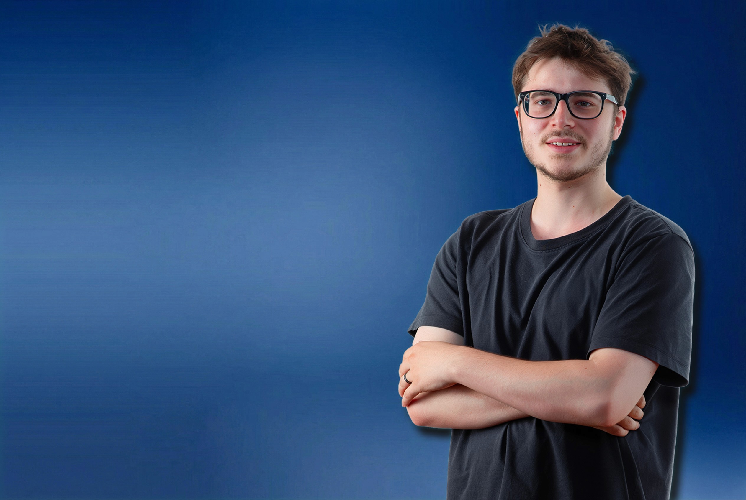 Porträt von mirudesign Gründer Mikail Althaus, der Werbeagentur aus Münster mit Brille und verschränkten Armen, lächelnd vor blauem Hintergrund.