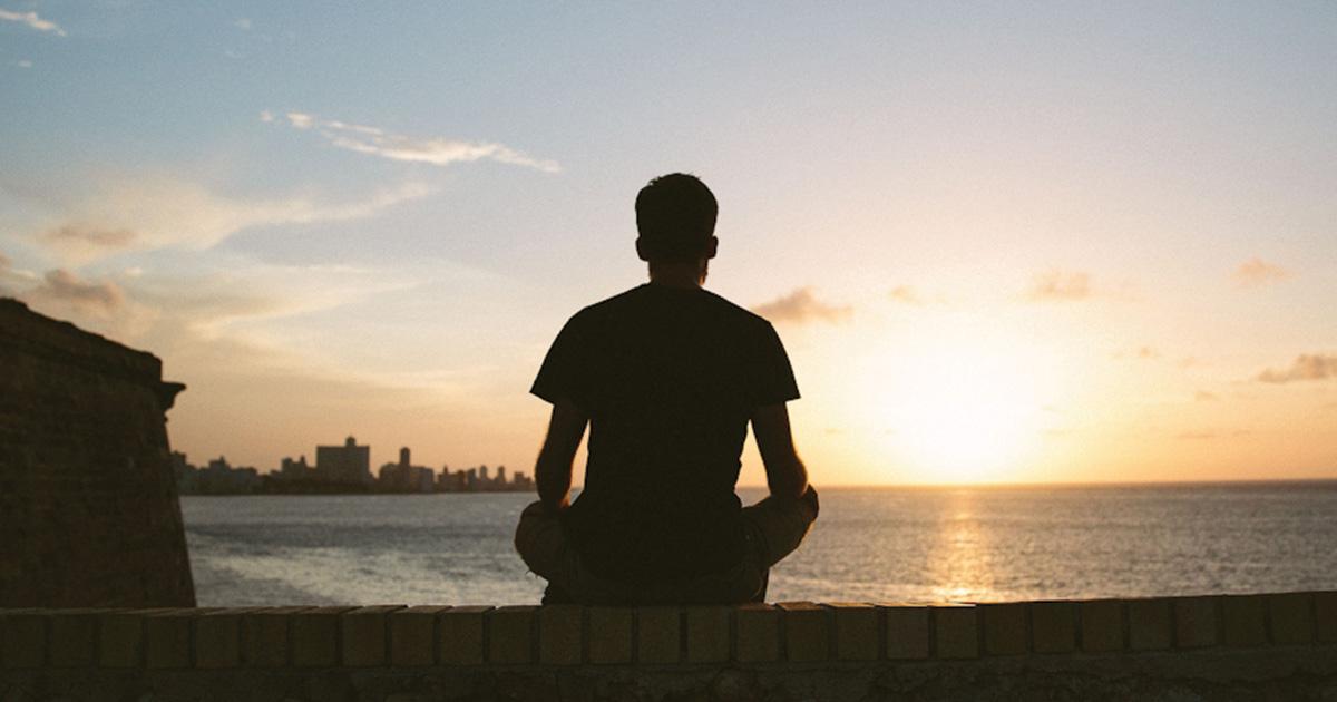 Person sitting quietly by the water at sunset, taking a moment to process their emotions.