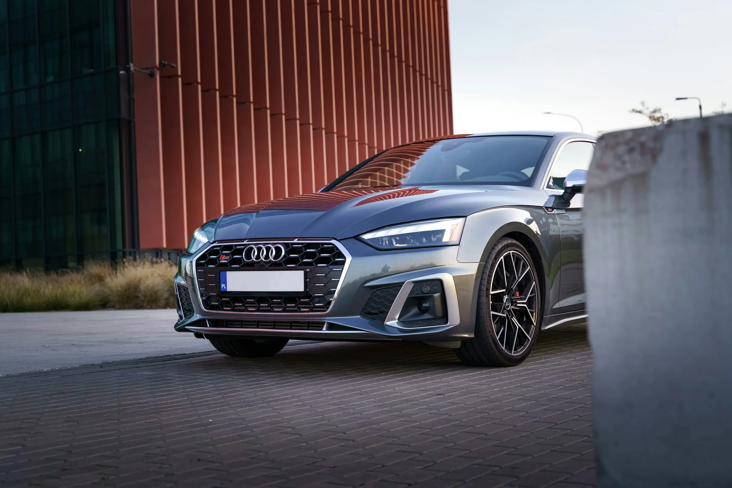 Gray Audi sedan parked on a paved area near a modern building.