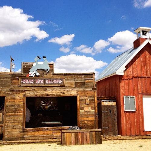 蓝天白云下，“死驴酒馆”标志的木制沙龙和一个红色谷仓。