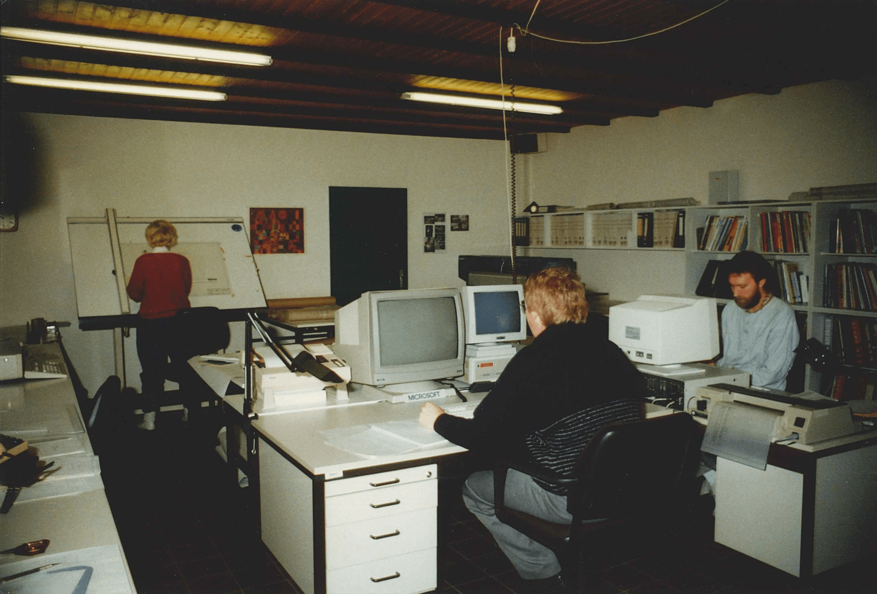 Büro aus den 90ern: Arbeitsplatz mit Computern, Zeichenbrett, Bücherregal. Retro Arbeitsatmosphäre.