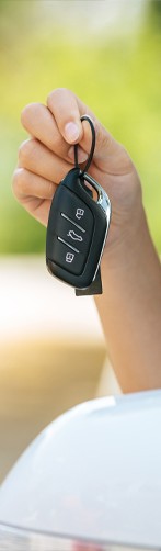 women's hand holding a car key outside of a white car with green background