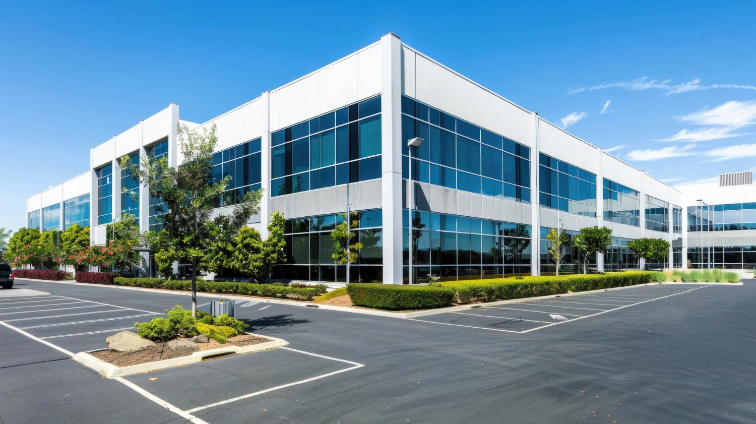 A person with glasses and a beard smiles warmly while working on a laptop at a desk. The setting is casual and relaxed, with a neutral background