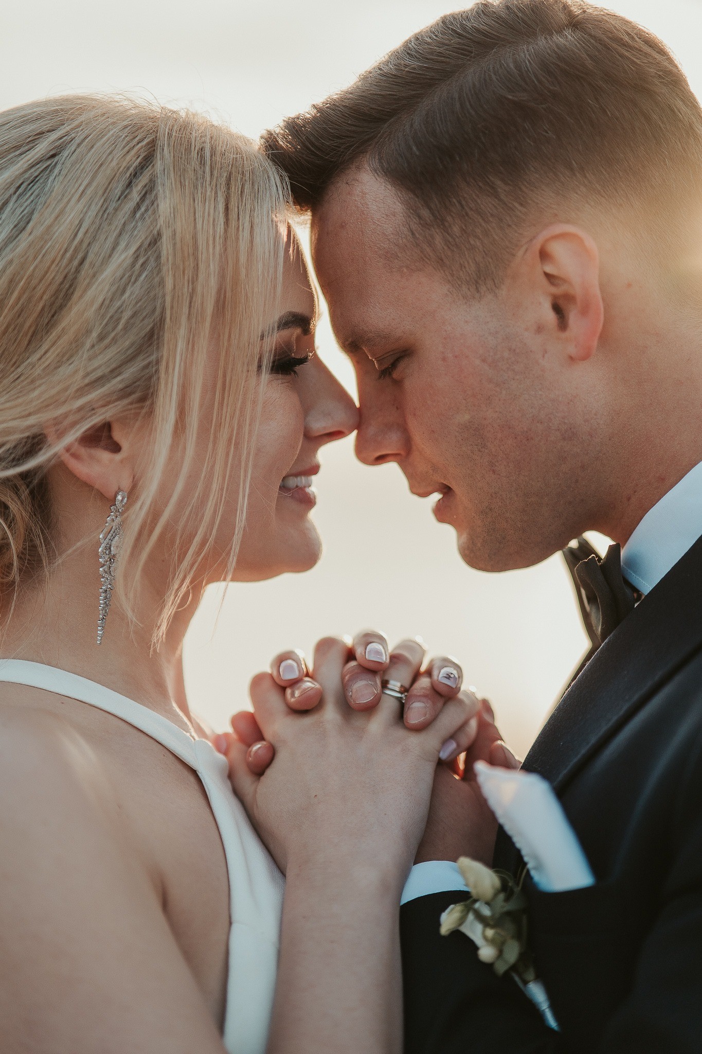 A couple in wedding attire walks hand in hand across a sunlit field.