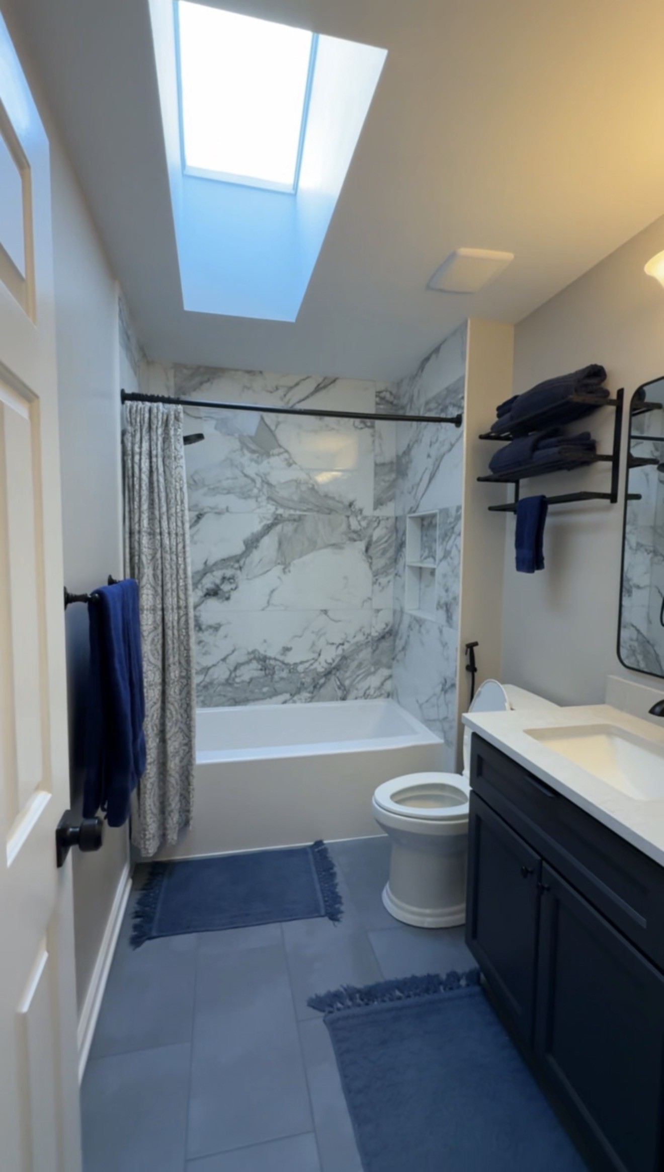 Tub-in-shower with marble-look tile walls and a skylight in the Weddington Hall bathroom remodel