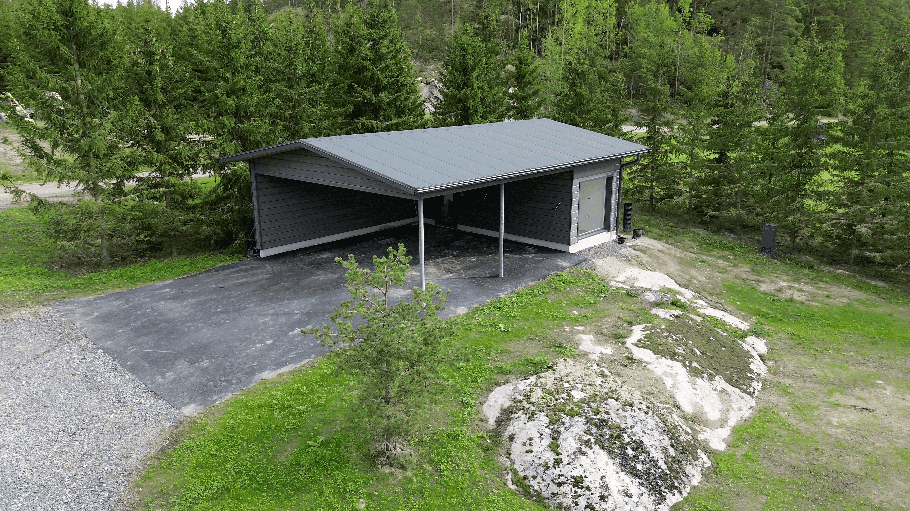 Carport viewed from the side. Paved road. Next to the cliff edge.