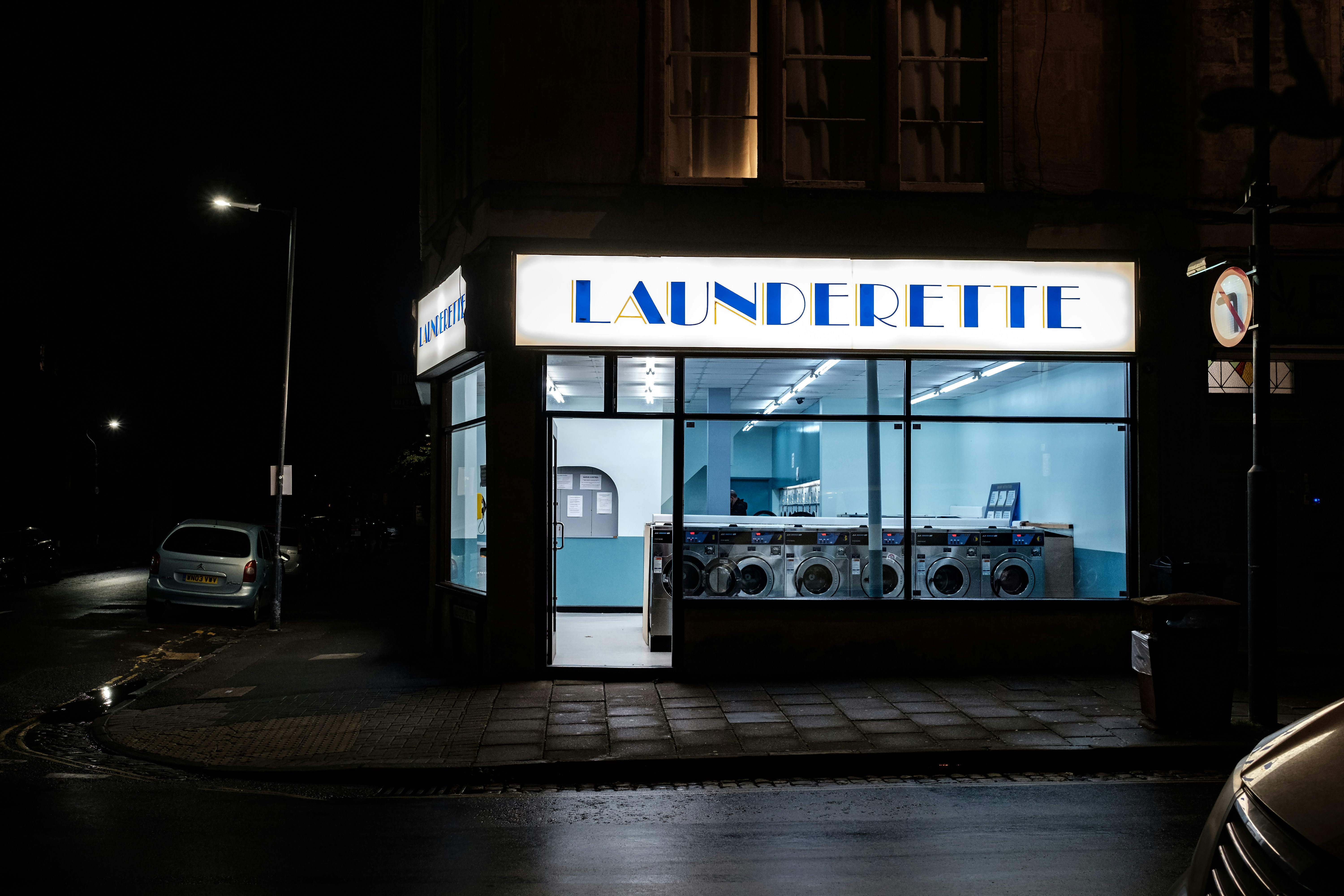A small launderette glowing on a dark street at night