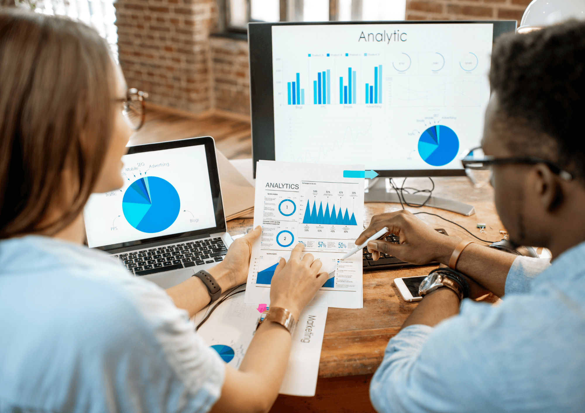 Two professionals analyze data charts and graphs on paper and computer screens, collaborating to derive actionable insights for strategic decision-making.