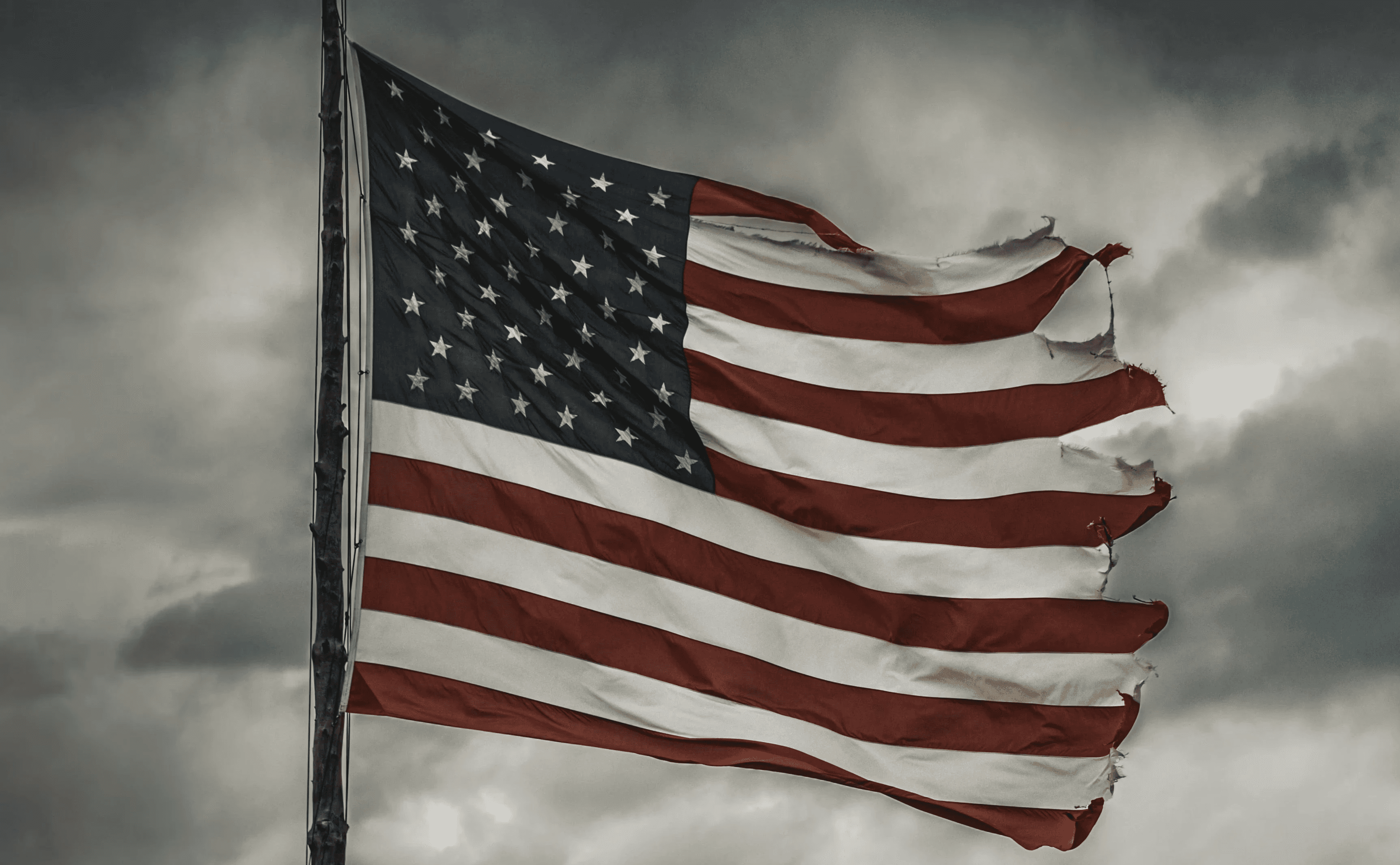 a large american flag flying in a cloudy sky
