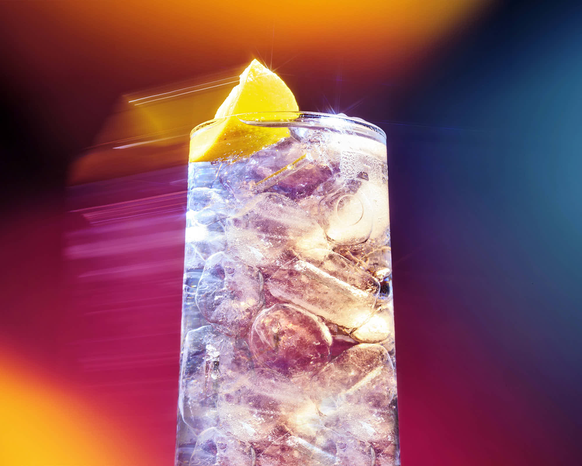 A colorful, illuminated ice-cold drink with a lemon wedge, set against a vibrant, blurred background.