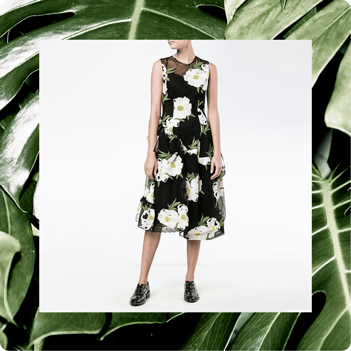 Woman wearing sleeveless black midi dress with white floral print, styled with black oxford shoes against tropical leaves