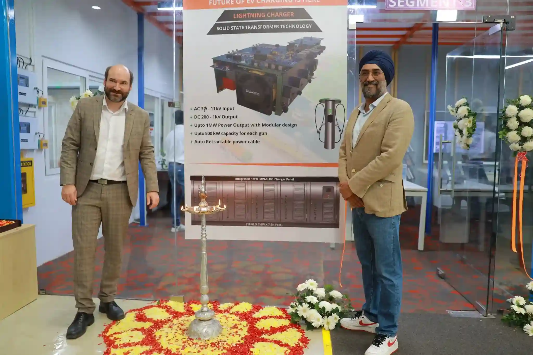 Two men stand in front of a poster and a lamp.