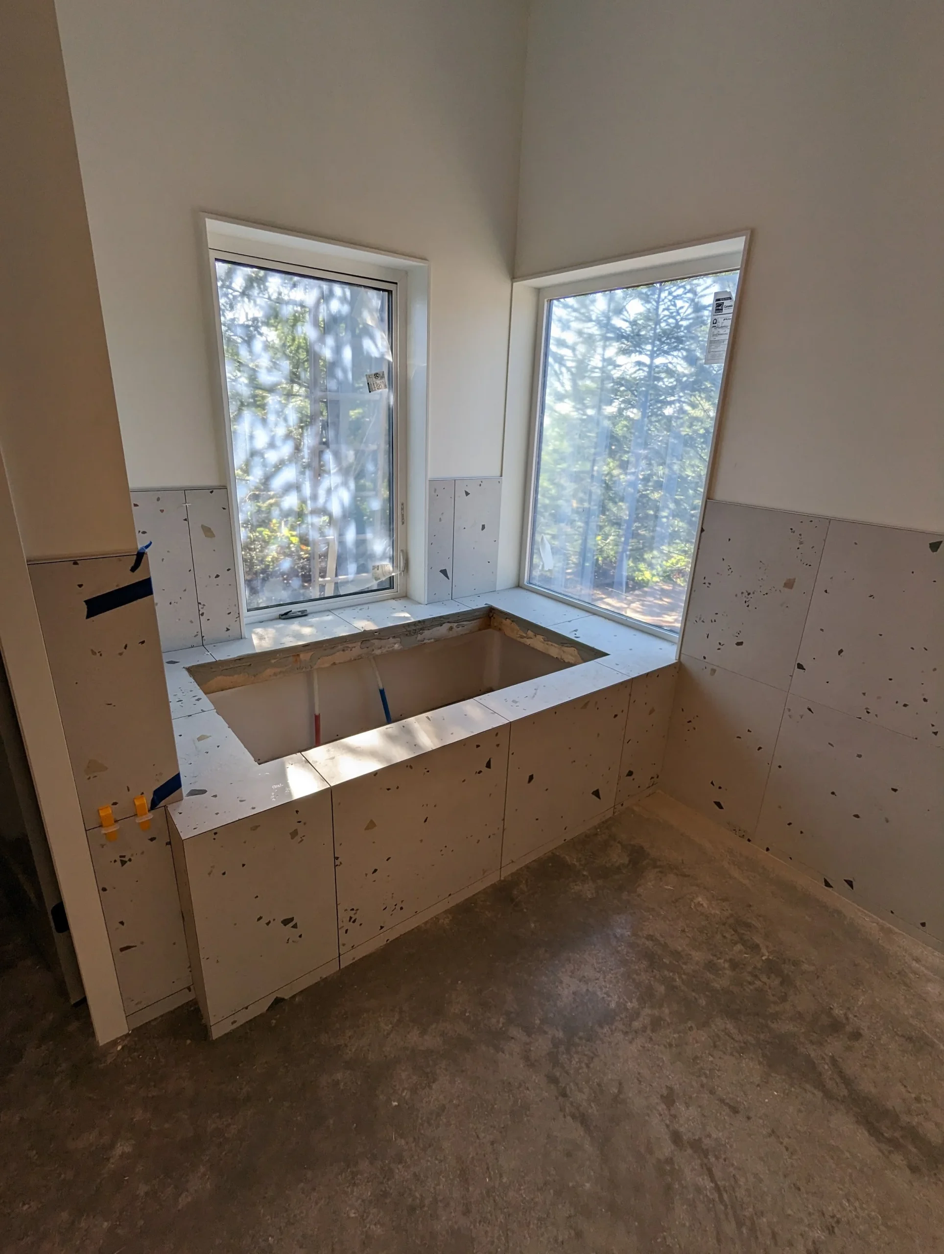 Modern two-story home with large glass windows, warmly lit interiors, and a balcony. Surrounded by trees and a manicured lawn at dusk. Cozy ambiance.