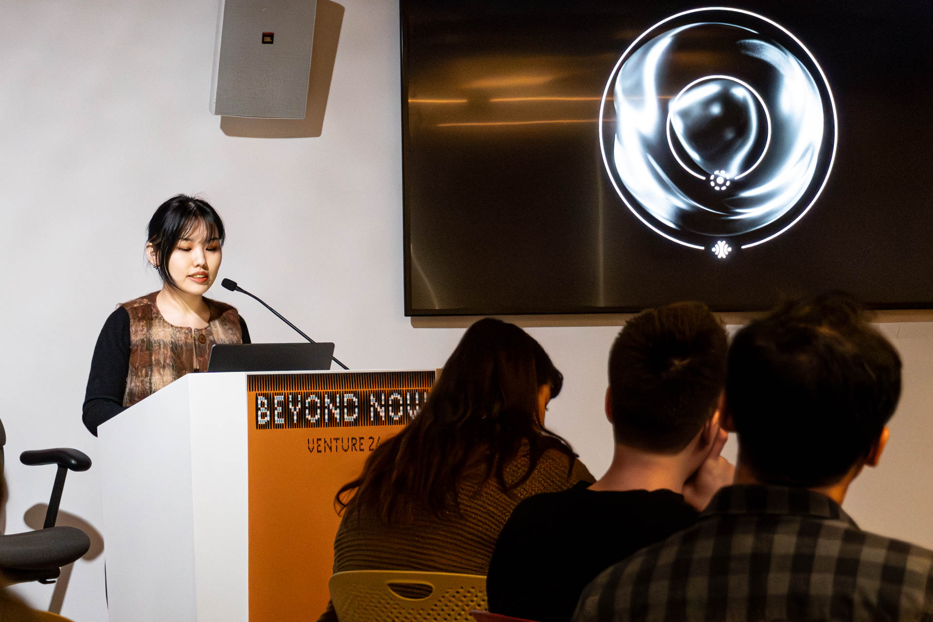 A lady at the podium giving a presentation to a class.
