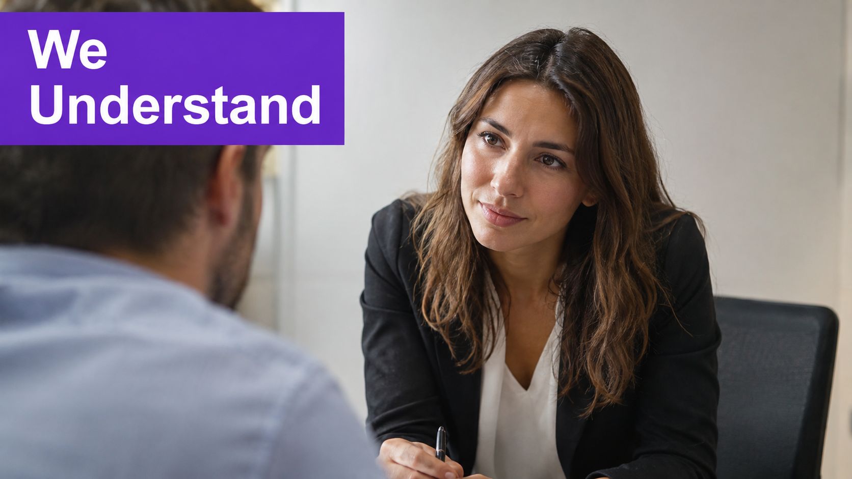 A professional woman in a business blazer listens attentively to a man during a business meeting.