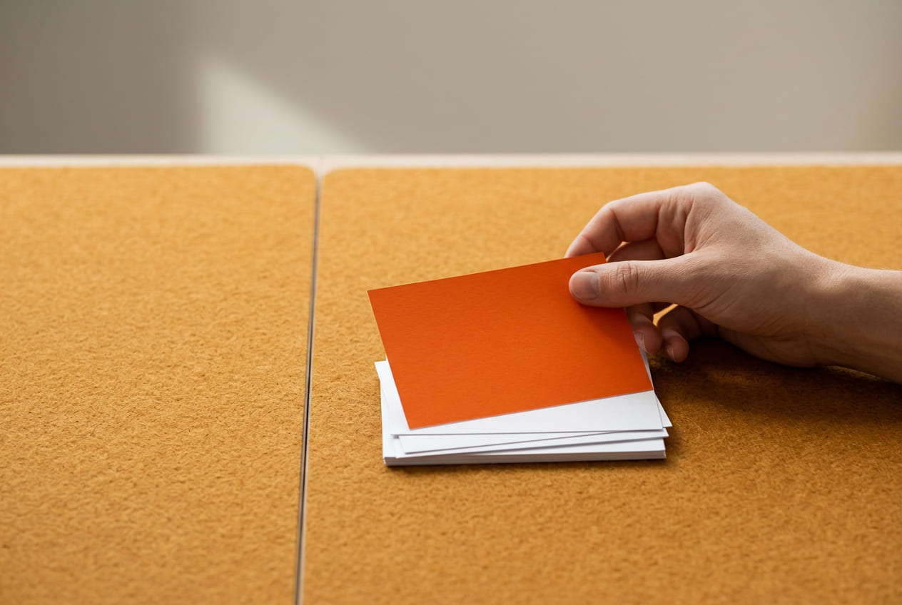 A hand places an orange index card on top of a stack of white cards on a felt surface