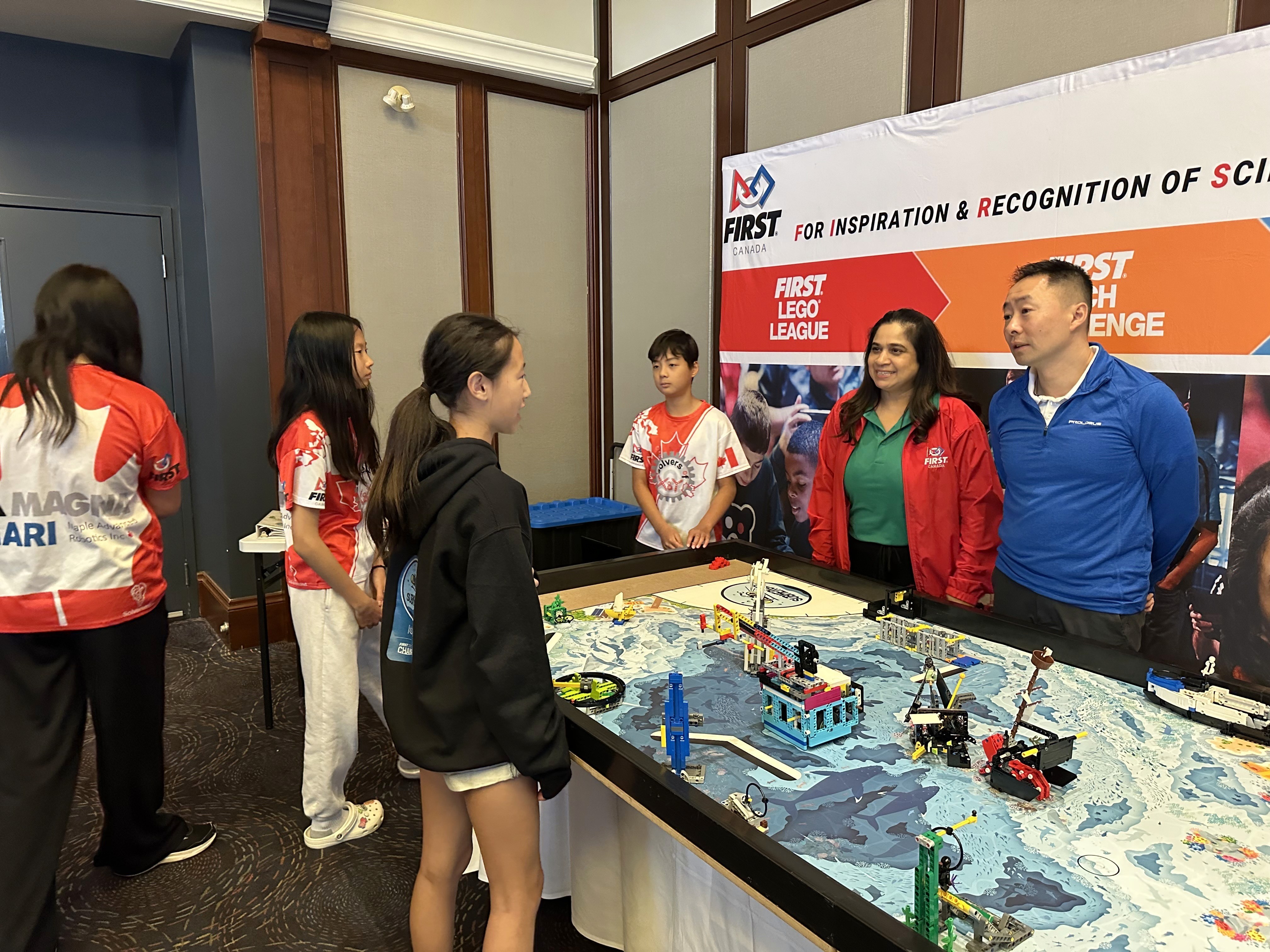 Renee Zhang from FLL Ontario Champion team Solvers of X & Y explains their robot and innovation project to Honda Canada Executive Steve Hui and FIRST Robotics Canada VP Arti.