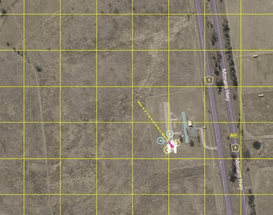 Aerial map view showing a drone’s flight path and waypoint markers overlaid on agricultural land with a road and grid reference system.