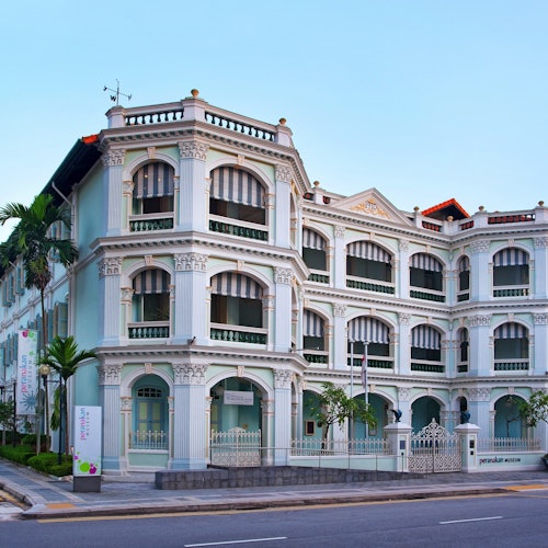 A multi-story building with arched windows and decorative columns, situated on a street corner under a clear sky.