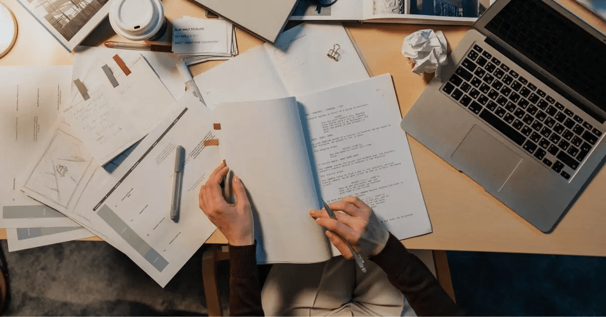 Researcher drafting a paper beside a laptop and notes