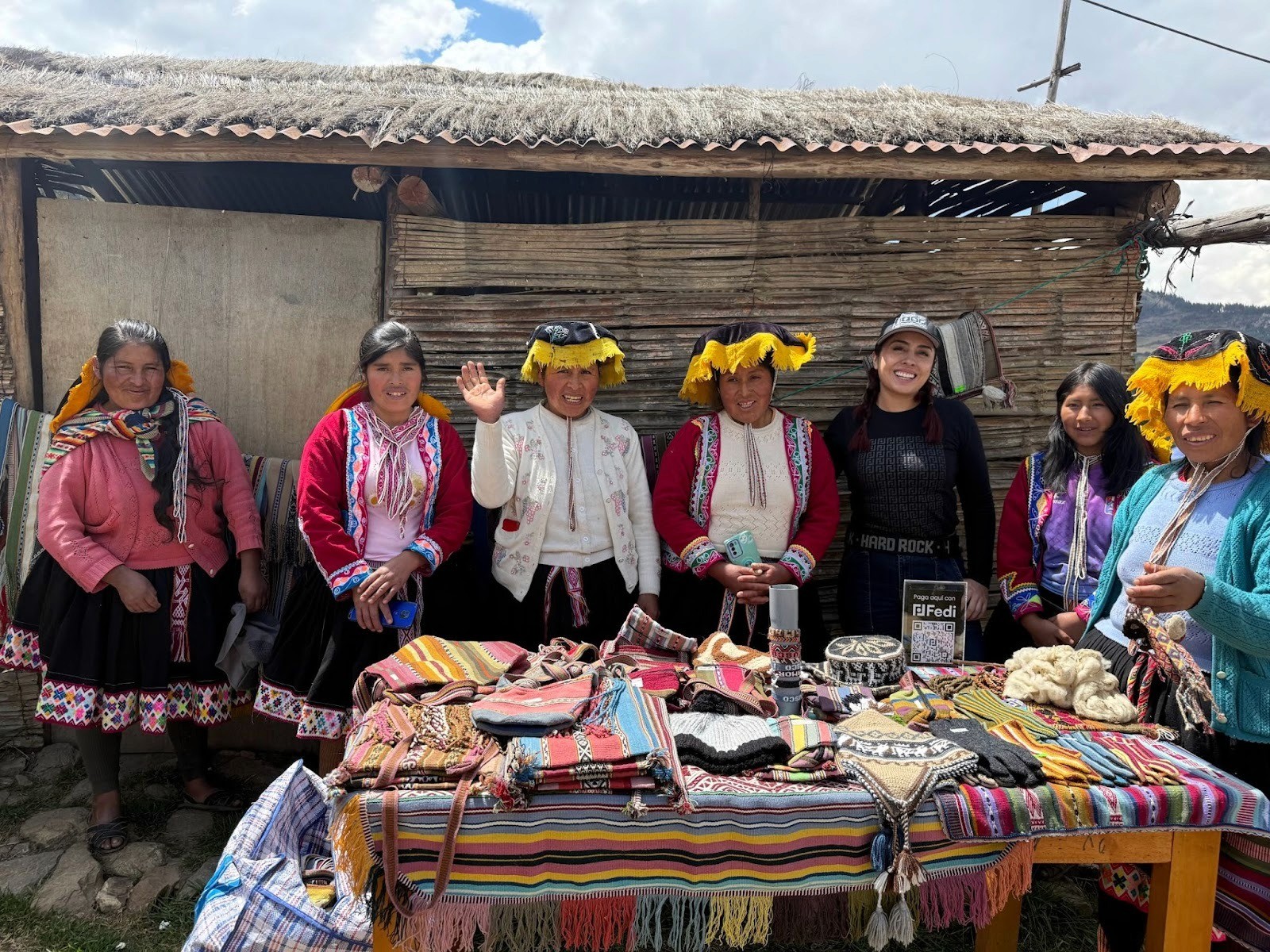 Lorena Ortiz, Fedi's Latin America Community Master, stands with six Andean artisans at a market stall in rural Peru, displaying colourful handwoven textiles and crafts. The community accepts Bitcoin payments via Fedi, with a "Paga aquí con Fedi" QR code sign visible on the table.