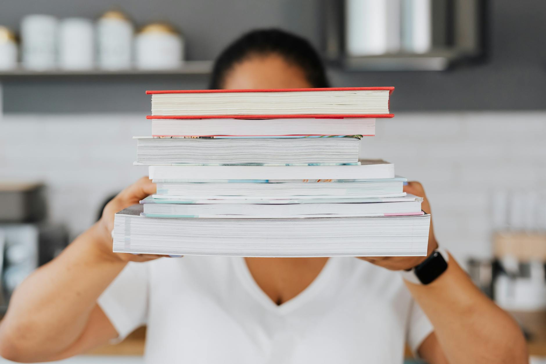 An overhead view of an organized wooden desk with a laptop, a pair of glasses, and a stack of hardcover workbooks.