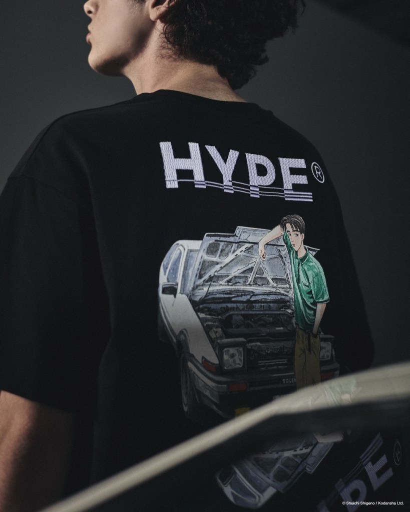 A close-up of a person wearing a black t-shirt featuring a graphic print of a character leaning on a car, with the word 'HYPE' prominently displayed on the back.