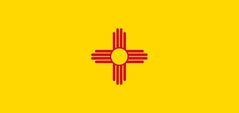 The image shows the New Mexico state flag, featuring a red Zia sun symbol with rays extending from a circle on a bright yellow background.
