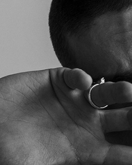 Black and white close-up of a person covering one eye with their hand, wearing a simple metal ring.