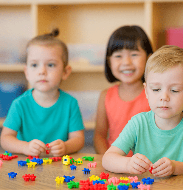 Three preschool children engaging with colorful building toys during a classroom activity