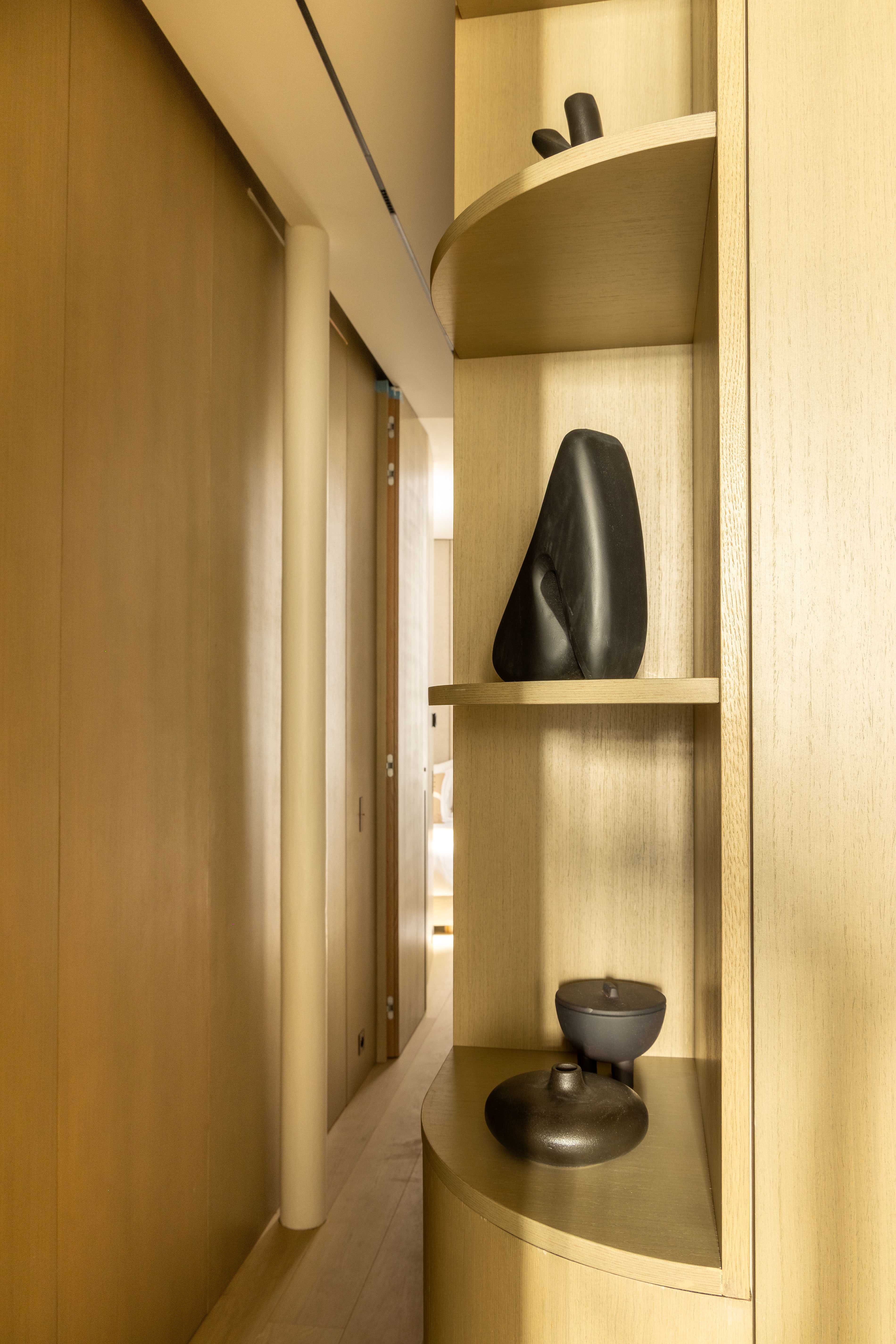 Étagère arrondie en bois clair avec sculptures noires décoratives dans un passage étroit