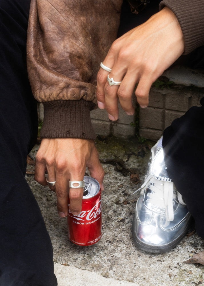 Person holding a Coca-Cola can on a concrete surface with a brick wall in the background.