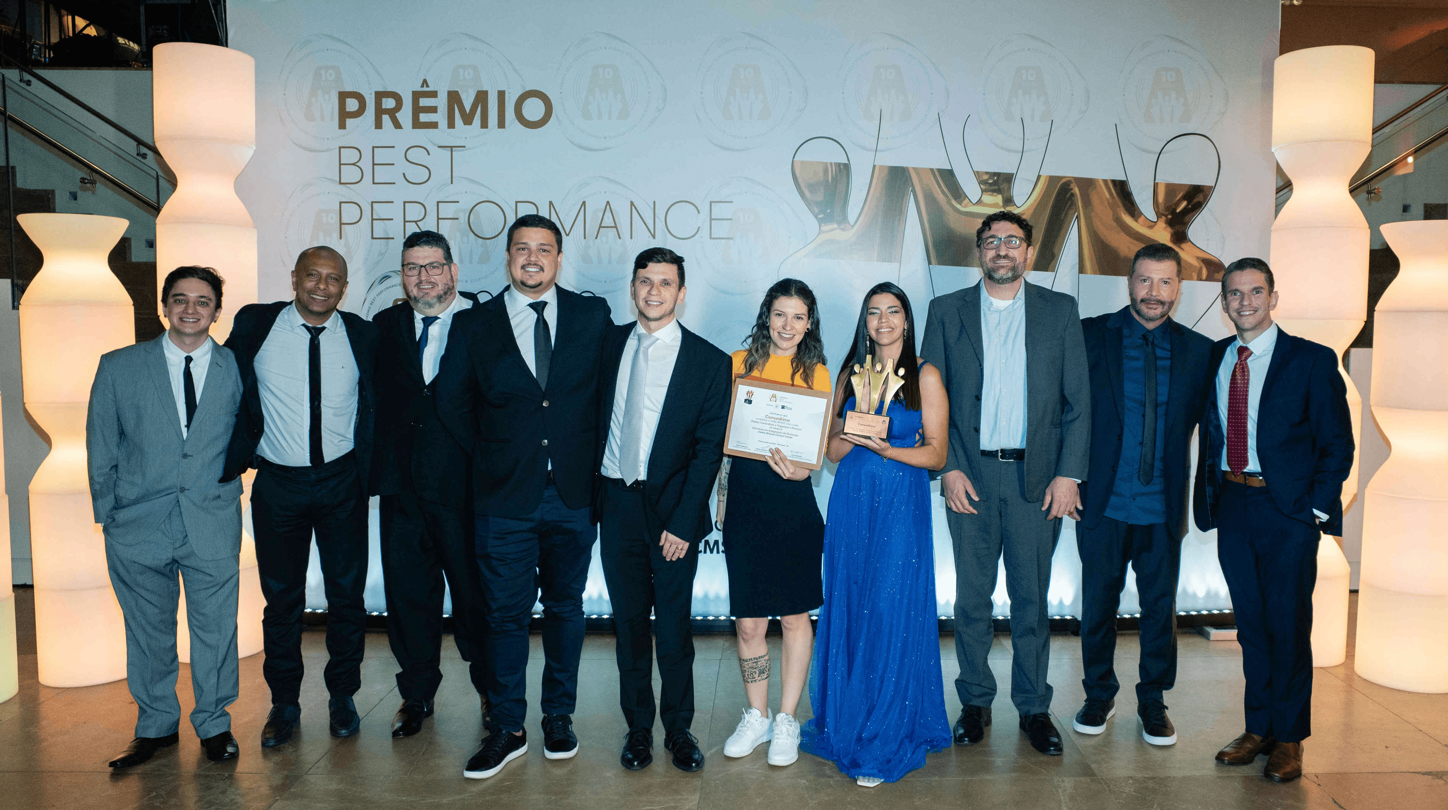 Executivos da Comunikime posando com troféu bronze e certificado no palco do Prêmio Best Performance 2025.