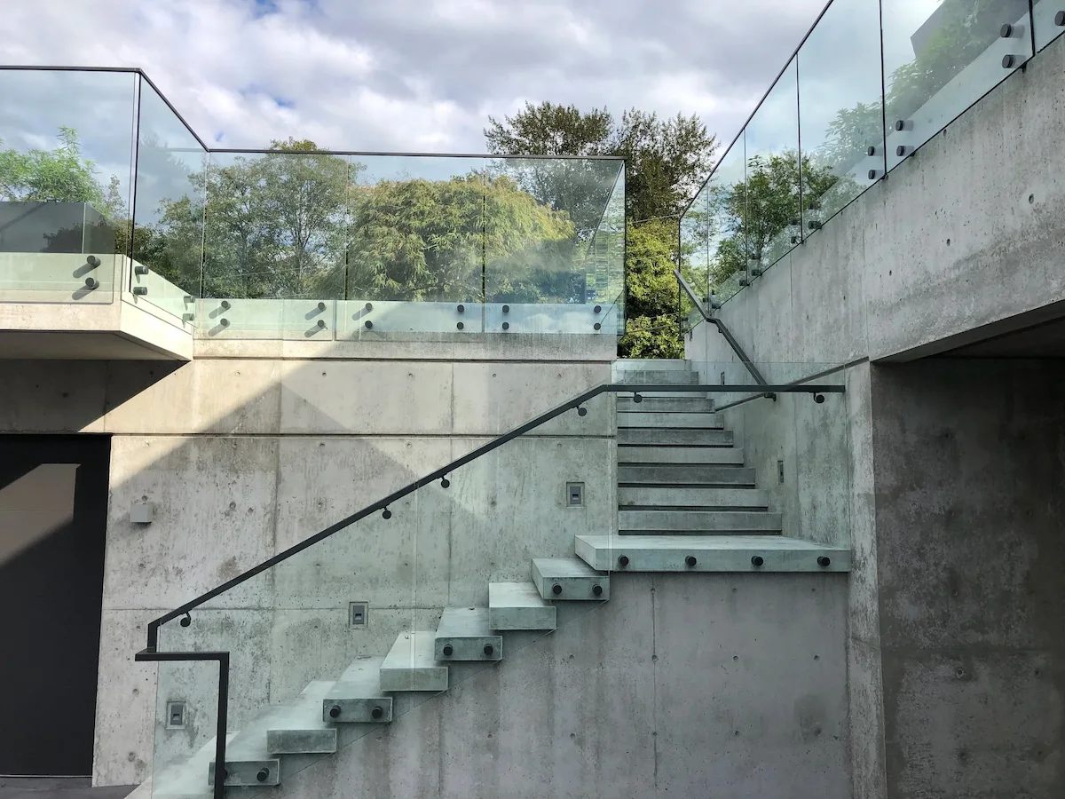 Institutional and public buildings glass railings installed along exterior concrete stairs, featuring clear glass guardrails with metal hardware to provide fall protection in a modern, accessible outdoor circulation area.