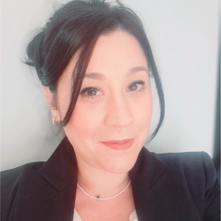 A smiling person wearing glasses and a patterned shirt stands against a plain white background.