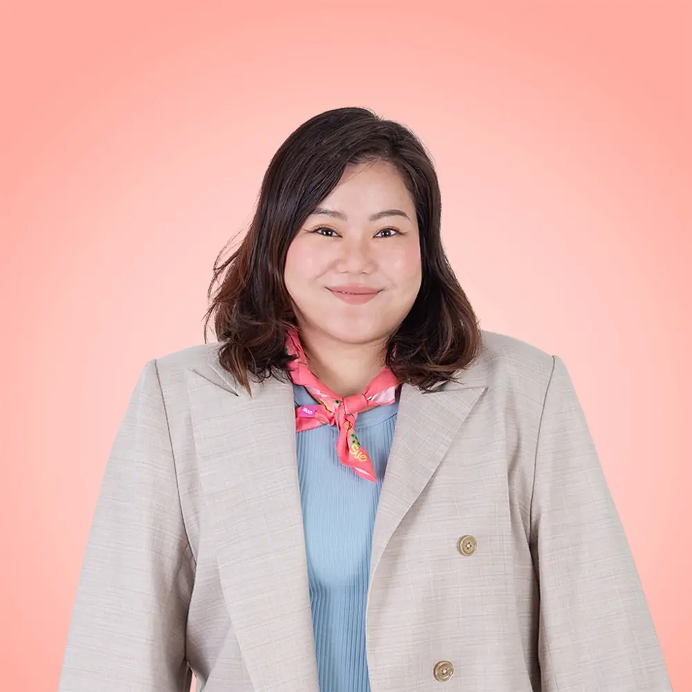 A smiling person in a black suit stands against a light blue background.